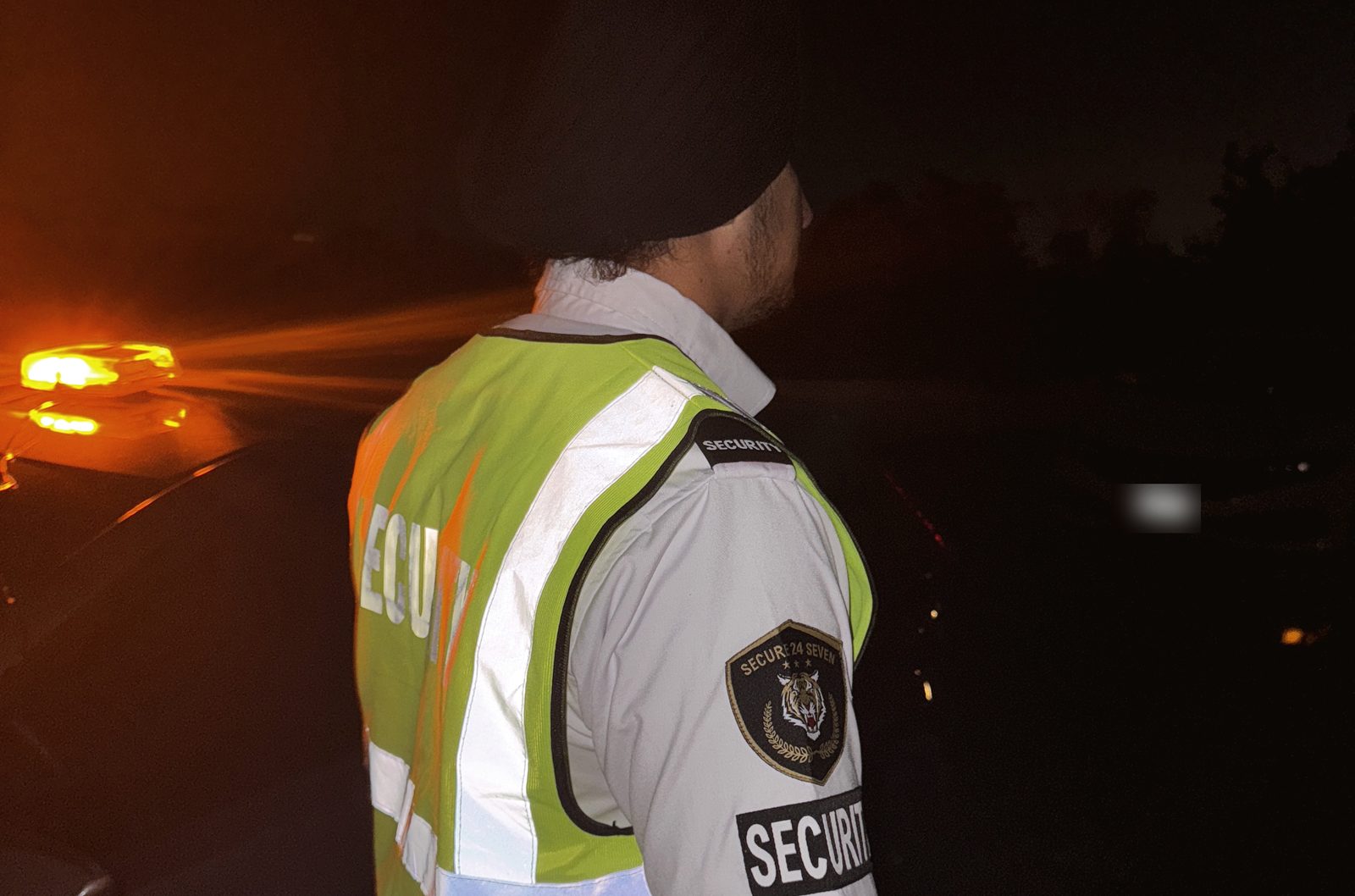 Secure 24 Seven guard responding at night beside a patrol vehicle